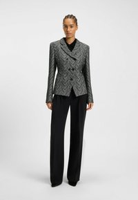 Houndstooth-mønstrede blazer i sort og hvid, med dobbeltknaplukning, kæbe kollet og lange ærmer. Parret med sorte bukser.