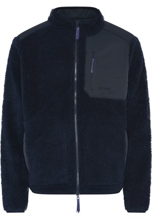 Marineblå fleecejakke med høj krave, lynlås foran og brystlomme til venstre med et mørkt stofpanel og logodetaljer.