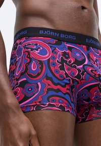 Horej mužský trup s farebnými kvetinovými a abstraktnými vzormi boxeriek s čiernym pásom s nápisom "BJÖRN BORG."