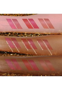 Schwatches von sechs Lippenfarben auf Armen, die verschiedene Schattierungen von Pink und Nude mit einem glänzenden Finish zeigen, beschriftet mit Namen wie "Electric Bloom" und "Divine Rose Glow."