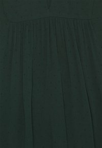 Abito verde scuro realizzato in tessuto leggero, caratterizzato da una superficie texturizzata con piccole macchie e dettagli plissettati lungo la gonna.