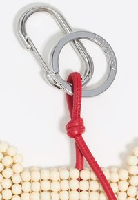 Beaded accessory with cream beads, red leather strap, and silver metal hardware. Features a keyring style with a knot detail.