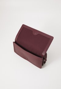 Bordeaux leren tas met een gestructureerde afwerking, voorzien van een klep sluiting en een open zak. Het interieur is van een gladde bordeaux stof.