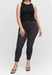 Top sin mangas negro con textura acanalada combinado con jeans ajustados gris oscuro. Los jeans tienen una cintura alta y una silueta ajustada, complementados con chanclas negras.