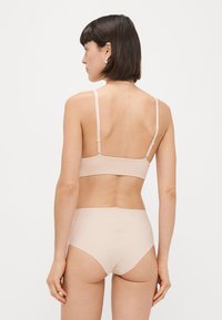 Nude donji veš set koji uključuje jednostavnu brusnicu s podesivim naramenicama i gaćice visokog struka, izrađene od glatkog rastezljivog materijala.