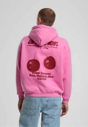 Rosa hættebluse med et grafisk motiv på ryggen af kirsebær og teksten "Sweet Summer. Ibiza, Mallorca, Nice ©2024." Blød bomuldsstof.