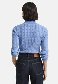Lichtblauwe kabelgebreide trui met een opstaande kraag; heeft ribgebreide manchetten en zoom, gecombineerd met donkere denim jeans met leren merklabel.