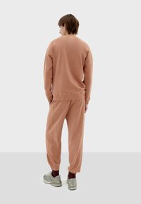 Light brown sweat set made of soft fabric; features a relaxed fit, ribbed cuffs, and tapered pants. Footwear includes gray sneakers with accents.