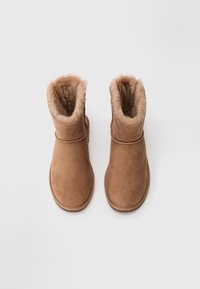 Bottines en suede marron avec une doublure douce et moelleuse, un bout arrondi et un design minimaliste. Présentent un détail de couture autour de la cheville.