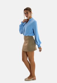 Lichtblauwe blouse met geplooide mouwen, gecombineerd met een tan suède minirok en beige instapschoenen. Casual, aansluitend silhouet.