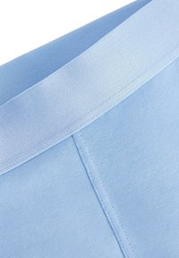 Tessuto blu chiaro con una texture liscia. Presenta una cintura elastica ampia e cuciture piatte per il comfort. Mostra un primo piano dei dettagli del capo.