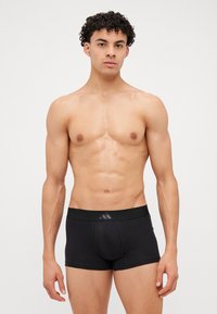 Schwarze Boxershorts aus elastischem Material mit breitem, elastischem Bund und einem dezenten Logo. Glatte Stoffoberfläche, figurbetontes Design, mittlere Oberschenkellänge, minimale Nähte.