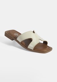 Sandalen met een glanzende, crèmekleurige kunstlederen bovenkant, met een uitsnedeontwerp en een bruine gevoerde voetbed, geplaatst op een lage blokhak.