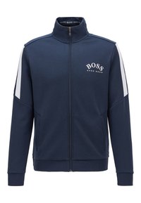 Chaqueta de chándal con cremallera en navy, fabricada en un material suave, con franjas laterales blancas y el logo "BOSS" en el pecho en blanco contrastante. Cuenta con dos bolsillos laterales.