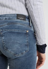 Tmavě modré džíny z denimu s mírně vybledlým vzhledem, s černou visačkou Mavi Jeans Co. na pase a designem zadní kapsy.