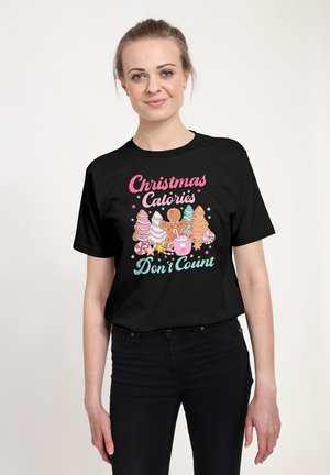Kvinde i sort T-shirt med juleslik og ordene "Christmas Calories Don't Count" med farverige bogstaver, står og smiler.