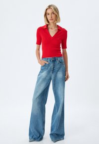 Polo rouge à côtes avec manches courtes associé à un jean large bleu clair, à taille haute et à la texture en denim délavée.