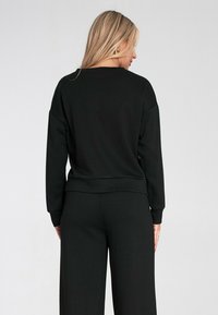 Czarna bluza dresowa o luźnym kroju, z długimi rękawami i okrągłym dekoltem, wykonana z miękkiego materiału. Model nosi pasujące czarne spodnie.