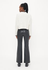 White ribbed cropped sweater with black trim, paired with black flared leather pants. Back view shows a smooth, sleek texture.