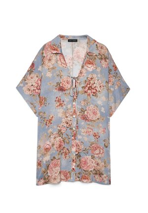 Camisa de manga corta con botones en azul claro con estampado floral en rosa y beige y detalle de lazo en el escote.