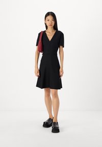 Vestido preto com mangas curtas, design em V, corpete ajustado e saia evasê. Combinado com uma bolsa bordô e sapatos de plataforma pretos.