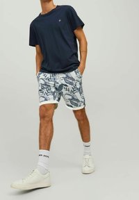 Camiseta de manga corta marina combinada con pantalones cortos blancos con un patrón de hojas azules, dobladillos enrollados, zapatillas blancas y calcetines blancos con texto.