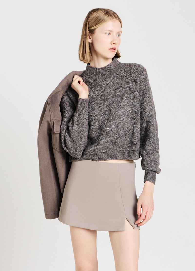Brown, textured, cropped sweater with a high neckline and loose sleeves paired with a beige mini skirt featuring a side slit.