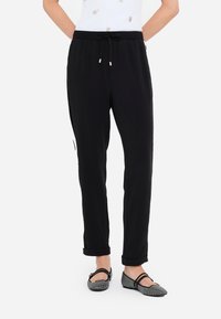 Pantalones de chándal negros con cintura elástica, cordón y bolsillos laterales; tejido elegante con una textura suave y puños ajustados en los tobillos.