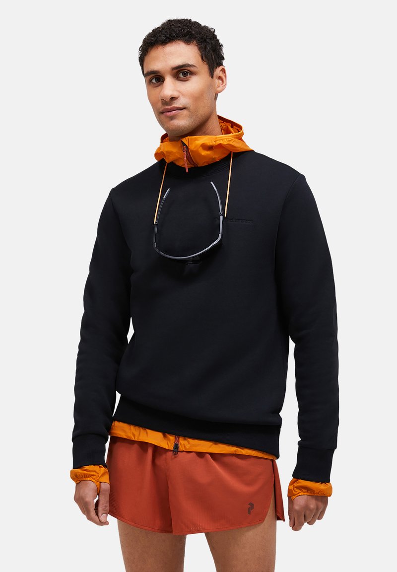 Melnā viesē ar oranžu kapuci, ar priekšējo rāvējslēdzēju. Modelis valkā oranžas šortus, ar saulessargiem, kas karājas no kakla.