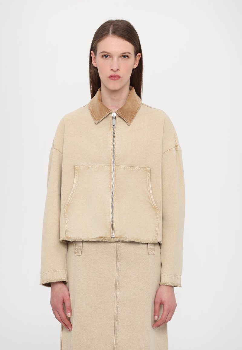Giacca beige corta con un morbido colletto in corduroy marrone, cerniera frontale e grandi tasche a toppa. Tessuto testurizzato con una vestibilità comoda.