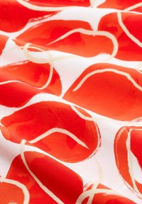 Tissu floral rouge avec des formes de pétales brillants et superposés, entourés de contours crème sur un fond blanc. Texture lisse avec des couleurs vives.