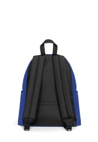 Mochila azul con correas negras, un asa superior y un bolsillo con cremallera. Presenta una forma redondeada y un material texturizado.