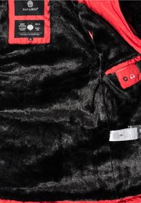 Sort jakke med kunstpelsfor og en livlig rød indvendig. Har et mærke med brandlogo og en lomme til høretelefoner med et symbol.