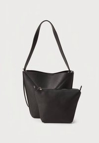 Černá kožená taška typu tote ve tvaru trojúhelníku, vybavená odnímatelnou zipovou kapsou, hladkou texturou a jedním ramenním popruhem.