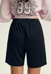 Czarne spodenki sportowe z elastycznym pasem i gładką fakturą, w połączeniu z różową bluzką z kwiatowym wzorem oraz numerem 89.