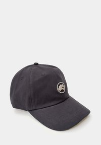 Gorra de béisbol negra con tejido texturizado, visera curva y un parche con logotipo circular en gris claro en la parte frontal. Ojetes metálicos para ventilación.
