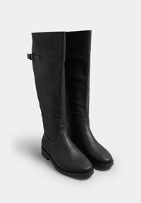 Botas negras hasta la rodilla, hechas de cuero suave, con un discreto detalle de correa, puntera redondeada y suela de goma plana para estabilidad.