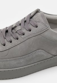 Grey suede sneaker with flat laces, seamless design, contrasting texture between upper and sole, and subtle stitching details.