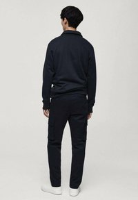 Marineblauwe poloshirt met lange mouwen en een kraag, gecombineerd met bijpassende cargobroek met zijzakken en witte sneakers. Gladde stoftextuur.