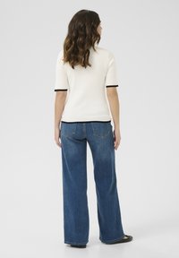 Haut blanc à manches courtes côtelé avec bord noir, associé à un jean bleu taille haute et large. Texture lisse, coupe décontractée et design basique.