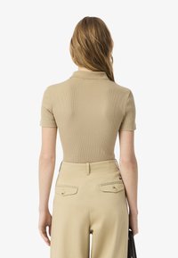 Polo shirt a costine beige con maniche corte, abbinato a pantaloni beige a vita alta con due tasche posteriori e delicati bottoni dorati.