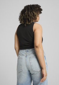 Zwarte geribde tanktop met een ronde halslijn, gecombineerd met lichtblauwe high-waisted jeans met twee achterzakken. Zacht materiaal en casual pasvorm.