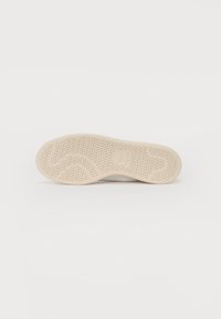 Suela de zapato en color beige con un patrón texturizado en forma de panal. Forma redondeada con un surco central, que presenta un pequeño grabado de logo.