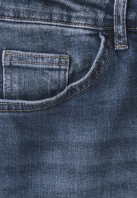 Granatowy dżinsowy materiał z przednią kieszenią, ozdobioną przeszyciami oraz delikatnym efektem wypłowienia, podkreślającym fakturę i wykonanie.