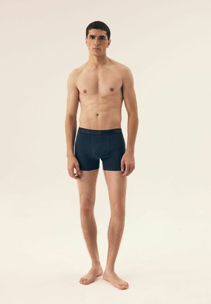 Blaue Boxershorts aus weichem, leichtem Stoff mit einem Punkte-Muster, elastischem Bund, der mit "HENDERSON" gekennzeichnet ist.