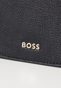 Portafoglio in pelle nera con texture che presenta un logo dorato "BOSS". La superficie ha una finitura a granulato con cuciture visibili.