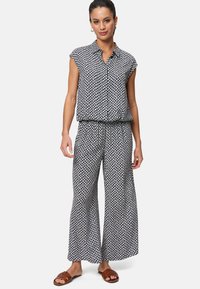 Camicia a maniche corte a righe blu navy e bianche con pantaloni larghi e svasati. Tessuto leggero con una superficie liscia. Sandali piatti indossati.