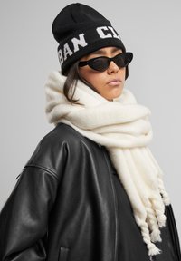 Beanie in maglia nero con testo "URBAN CLUB", sciarpa crema con texture morbida e giacca di pelle nera, caratterizzata da una vestibilità rilassata e chiusura con zip.
