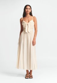 Maxi sukienka w jasnym beżowym kolorze z czarnymi kropkami, z detalem w postaci kokardy na biuście, regulowanymi ramiączkami i zwiewną spódnicą.