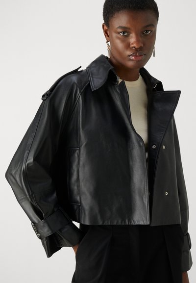 Μαύρη δερμάτινη κοντή ζακέτα με μεγάλο γιακά, κουμπάκι μπροστά και ρυθμιζόμενους καρπούς. Λείο υφή με ελάχιστες λεπτομέρειες από μεταλλικά στοιχεία.